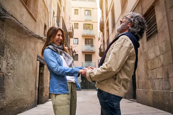 Adult retired attractive couple hand in hand laughing together on city street. Mature Caucasians enjoying reunion in person. Happy and cheerful people on romantic lovers weekend getaway having fun