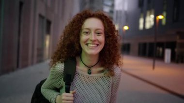 Beyaz, genç ve güzel bir kız. Dışarıdaki şehir kameralarına gülerek gülüyor. Nesiller boyu dost canlısı kızıl saçlı kadın arka planda şehir ışığıyla caddede neşeli poz veriyor. Boşluğu kopyala 
