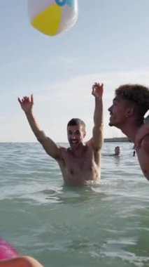 Mayolu, dikey bir grup genç arkadaş deniz kıyısında vakit geçiriyorlar ve mavi gökyüzünün altında bir plaj topuyla oynuyorlar. İnsanlar yaz tatillerinde eğleniyor.