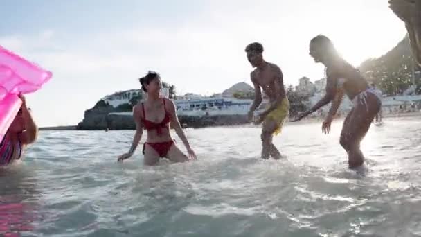 一群穿着泳衣的年轻朋友在海滩上互相泼水玩乐 不同的人在暑假里玩着Gen Z的水上运动 — 图库视频影像
