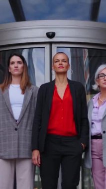Dikey video. Bir grup başarılı ve gururlu iş kadını kameraya doğru yürüyor. Ofis binası dışında ciddi ve yetkin yetişkin profesyonel kadın ortaklar.