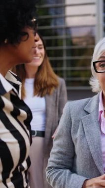 Dikey. Bir ofis binasının önünde resmi takım elbiseli, çeşitli profesyonel iş kadınlarıyla tanışmak, sohbet etmek ve finans merkezinde el kol hareketi yapmak.