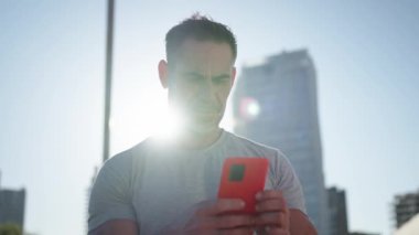 Olgun beyaz kaslı adam cep telefonu kullanarak ayakta duruyor. Spor elbiseli bir erkek ciddi bir hücrede kayıyor. Dijital ekrana bağlı sağlıklı insanlar. Mercek parlaması 