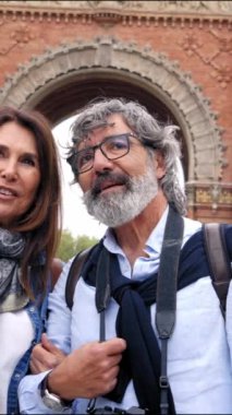 Dikey. 60 'lı yaşlarındaki olgun bir çift Avrupa sokaklarında sarılıp sohbet ederek yürüyor. Mutlu yaşlı çift tatilde ya da hafta sonu kaçamağında birlikte eğlenmek için bir turisti işaret ediyor.