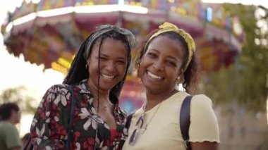 İki güzel Afro-Amerikan kadın, bir lunaparkta birbirlerine sarılıp bakarken mutlu mesut duruyorlar. Gülen lezbiyen çift eğleniyor ve eğleniyor