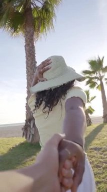 Dikey. Genç ve mutlu bir Afrikalı kadının sevgilisini çektiği pozu takip et. Egzotik tropik plajda erkek eli tutan gülümseyen kız. Aşk insanlar yaz tatilinde seyahat eder. Bakış açısı ve yavaş çekim