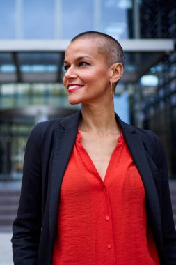 Dikey. Modern stil sahibi Kafkasyalı, resmi takım elbiseli, açık havada duran yetişkin bir iş kadını. Güçlü ve güçlü bir kadın. Tıraşlı kafasıyla mutlu. Gülümsüyor.