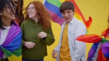Dansçılar ve heyecanlı genç LGBT 'ciler gay onur günü festivalinin tadını çıkarıyorlar. Bir grup neşeli arkadaş, gökkuşağı bayraklı sarı bir duvarın önünde birlikte eğleniyorlar. 