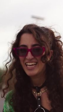 Dikey. Güneş gözlüklü, mutlu, beyaz bir kadın LGBT haklarını kutluyor. Diğer nesiller açık havada, zıplıyor ve dans ediyorlar. Gay Gurur Ayı Şenlikleri