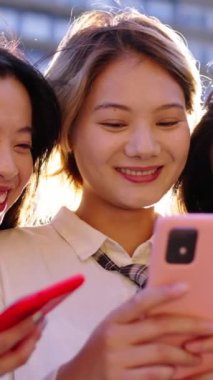 Dikey üç gen z güzel Çinli kadınlar mutlu bir şekilde cep telefonundan komik videolar izliyorlar. Genç ve güzel Asyalı bayan arkadaşlar birlikte oturup güneşli günün tadını çıkarıyorlar. Dışarıdaki hücreleri neşeli görünüyor.