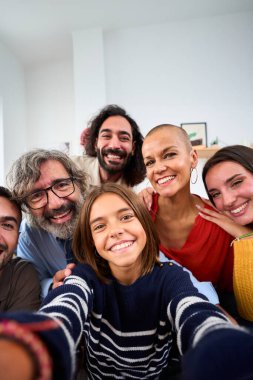 Dikey. Neşeli, beyaz bir aile, gülümseyip kucaklaşıyorlar ve içeride selfie çekiyorlar. Üç nesil boyunca beyaz insanlar evlerinde ön kameraya baktılar. Ev hayatındaki mutlu insan ilişkileri