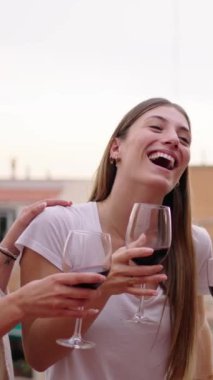 Dikey. Genç, çok ırklı, neşeli bayan arkadaşlar kadeh kaldırıyorlar, kırmızı şarap içiyorlar ve yaz partisini dışarıda kutluyorlar. Neşeli kadınlar çatıda eğleniyor. Mutlu kızlar birlikte tatilde. 