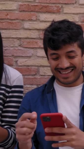 垂直的 多种族微笑团体年轻的一代在砖墙上一起使用手机室外 快乐的朋友们看着手机享受社交媒体的内容 快乐的人 对科技上瘾 — 图库视频影像