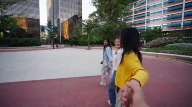 POV üç neşeli Asyalı kadın gülümsüyor ve şehir parkında el ele koşuyorlar. Bir grup genç Çinli arkadaş birlikte gezintiden zevk aldıkları için heyecanlılar. Mutlu insanlar dışarıda vakit geçirir.