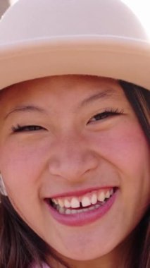 Kameraya neşeyle gülümseyen Asyalı genç kızın dikey yakın çekimi. Çinli bir kadın güneşli yaz tatilinde neşeli bir poz vererek güler. Güzel mutlu kadın.