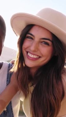 Güneşli havada gülümseyen kameraya bakan üç çok ırklı güzel kadının dikey görüntüsü. Nesiller boyu güzel bayan arkadaşlar yaz tatilinde birbirlerine sarılıp mutlu mesut poz verirler.