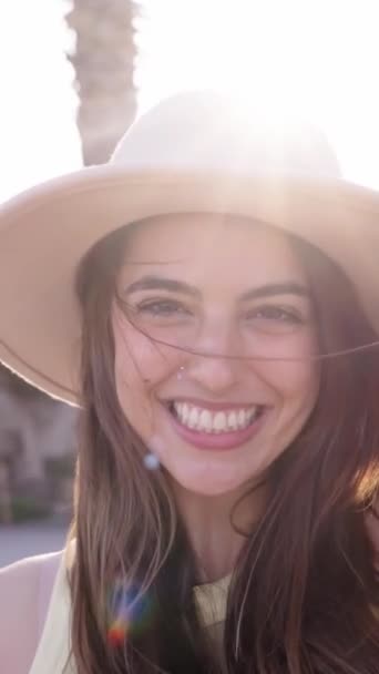 垂直的 迷人的白种人一代年轻姑娘开心地望着镜头笑着 在阳光灿烂的暑假里 漂亮的女人快乐地站在户外 戴帽子的漂亮的快乐女人 — 图库视频影像