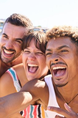 Dikey. Sahilde selfie çeken üç farklı cinsiyet ve ırk birlikte gülümseyip eğleniyorlar. Yaz tatili ve tatillerinin tadını çıkaran genç nesil z 'lerin portresi