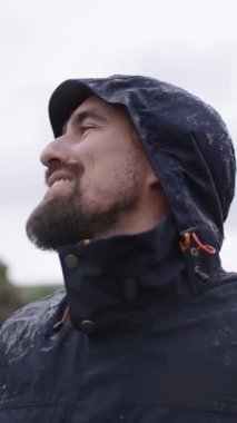 Dikey. Koyu mavi Mackintosh 'lu, gülümseyen beyaz bir adam mekâna bakıyor. Mutlu yakışıklı erkek doğada özgürlük ve huzur hisseder. Yağmur yağarken tatilin tadını çıkarır.