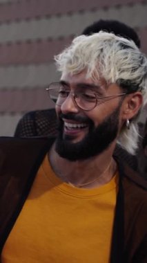 Caddede dans eden mutlu bir grup insanın dikey fotoğrafı renkli gökyüzünün altında gökkuşağı bayrakları taşıyor, eğlence ve eğlence dolu neşeli bir etkinliğin keyfini çıkarıyorlar.