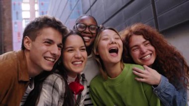 Çok ırklı grup öğrencileri, üniversite kampüsünde eğlenirken birlikte bir şeylere heyecanlı bir şekilde sarılıyorlar. Topluluktaki çeşitli neşeli genç arkadaşlar büyük gülücüklerle dışarıda eğleniyorlar.
