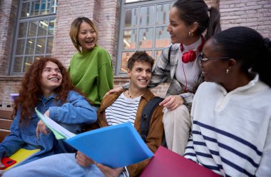 Bankta oturan bir grup mutlu öğrenci üniversite kampüsünde çalışma kitaplarıyla bir araya geldi. Sınıf arkadaşları çok ırkçı gençler gülüyor ve eğleniyorlar.