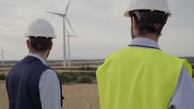 Mühendisler işçi grubu rüzgar santrali birlikte yürüyorlar. Sarı yelek ve miğfer giyip değirmeni planlıyorlar. Yel değirmeni çiftliğinde donanımlı çalışma araçları var. Profesyonel teknisyenler.