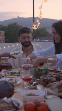 Dikey video. Akşamki etkinlikte, çatıdaki bir terasta oturan farklı arkadaşların yiyip içmesi. Kutlama için mutlu insanları bir araya toplayıp Akdeniz yemeği yiyeceğiz.