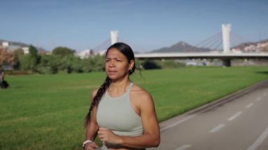 Şehir parkında koşan Latin, formda genç bir kadının ağır çekimleri. Sağlıklı vücut için kardiyo sporu dışında kadın çalışması. Sağlıklı insanlar dışarıda disiplinli eğitimdeler.