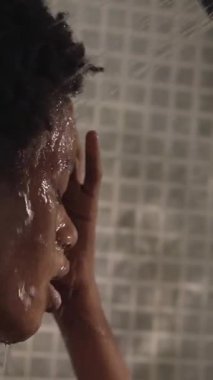 Dikey. Genç siyah afro kadın evde dinleniyor. Afro-Amerikalı kadınlar banyoda saçlarını ve saçlarını ıslatır. Sabahları ev içi temizlik kavramı.