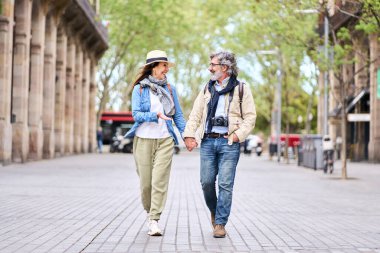 Mutlu yetişkin Kafkasyalı turist çifti. Birbirlerine bakıyorlar. Sokakta el ele yürüyorlar. Olgun insanlar romantik kaçamakların tadını çıkarıyorlar. Olumlu ilişkiler ve emekli bahar tatilleri