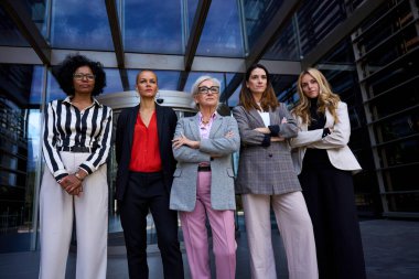 Düşük açı. Ofis binası dışında farklı yaş ve ırktan ciddi iş kadınlarının oluşturduğu bir ekip kurup haberleşiyorlar. Resmi takım elbiseli profesyonel kadın girişimciler.