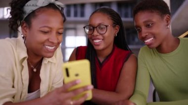 Gülümseyen, konuşan ve cep telefonu kullanan bir grup Afro-Amerikan kadın. Siyahi bayan arkadaşlar kapalı mekanda mutlu bir şekilde toplanıyorlar. Z neslinin teknolojisine bağımlılık
