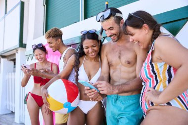 Mayo giyen ve duvara yaslanmış cep telefonu kullanan neşeli, çok kültürlü bir arkadaş grubu. Nesiller boyu insanlar yaz tatili boyunca hücrede birlikte komik videolar izleyerek gülüyorlar.