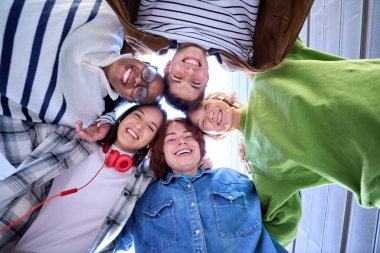 Low angle. Group of happy, smiling, multiracial classmates students gathered in a circle looking at camera hugging in celebration. Community of people in university campus and friendship concept