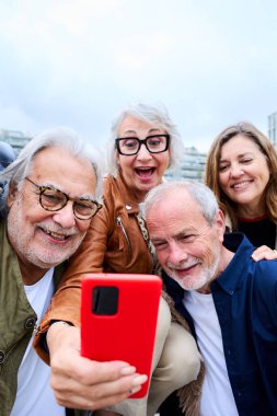 Dikey. Grup mutlu yaşlılar cep telefonlarını açık havada birlikte kullanıyorlar. Yaşlı arkadaşlar ve gülümseyen büyükanneler merkez nezarethanede. Olgun eski dostlar teknoloji bağımlılığı