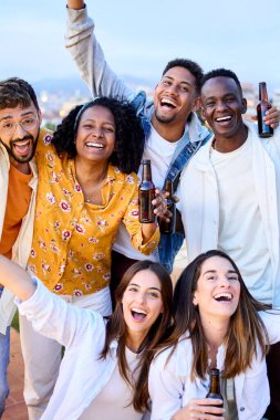 Dikey. Çeşitli heyecanlı arkadaşlar tavan arasındaki barbekü partisinde bira içerek kutlama yapıyorlar. Akşamları terasta kollarını kaldıran gençlerin portresi. Neşeli meslektaşlar eğleniyor