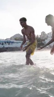 Mayolu bir grup genç arkadaşın sahilde birbirlerine su sıçratırken eğlendikleri dikey görüntüler. Yaz tatili boyunca çeşitli insanlar su oyunları oynayabilir.