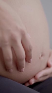 Dikey. Spor giyim giymiş, yoga pozu veren, tanınmayan hamile, beyaz kadın. Beyaz kadın kocaman karnına elleriyle dokunuyor. Bebek bekleyen fitness insanları.