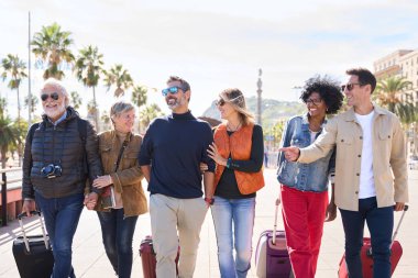Bir grup gülümseyen orta yaşlı arkadaş bavullarını Avrupa sokaklarında birbirine bakarak tasasız bir şekilde yürüyorlar. Çeşitli mutlu olgun insanlar seyahatlerinin tadını çıkarırlar.