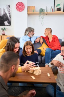 Dikey. Heyecanlı çok nesilli aile toplantısı evde Jenga oynuyor. Beyaz insanlar birlikte ev yaşamının masa oyunlarını oynuyorlar. Bir kadın kuleden bir odun parçası alıyor ve düşüyor.
