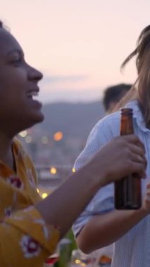 Çatıdaki barbekü partisinde genç ve mutlu grup dansçılarının dikey videosu. Heyecanlı insanlar atlıyor. Akşamları barbeküde bira içerek eğleniyorlar. Öğrenciler yaz tatilini kutluyor.