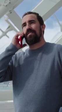 Dikey. Valencia 'daki bilim parkında cep telefonu kullanan yakışıklı bir beyaz adam. Genç yetişkin dışarıda gezici bir araçla konuşuyor. Telefona cevap veren erkek. İletişim kuran insanlar.