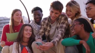 Bir grup Kafkasyalı genç dışarıda cep telefonundan gülümseyen videolar izliyorlar. Yeni nesil Z öğrencileri üniversite kampüsünde cep telefonlarını izlerken eğleniyorlar.