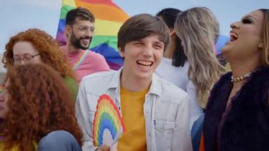 Bir grup insan gökkuşağı bayrağının önünde gülümsüyor ve işaret ediyor. LGBT 'nin mutlu bir gününü paylaşıyorlar. Açık havada eğleniyorlar.
