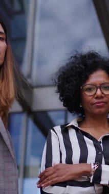 Dikey alçak açı. Resmi takım elbiseli ciddi iş kadınlarından oluşan bir grup bina ofisinin önünde yan yana kameraya bakıyor. Güçlü kadın girişimciler kollarını kavuşturdular.