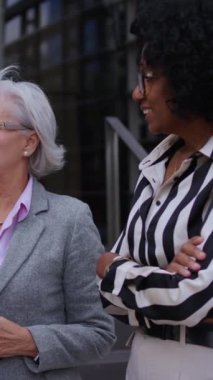 Dikey video. İş dünyasından çeşitli yaş ve ırktan kadınlar ofis binasının dışında konuşuyorlar ve günlük toplantılar yapıyorlar. Resmi takım elbiseli profesyonel kadın girişimciler.