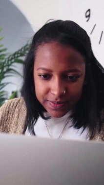 Dikey gülümseyen siyah kadın evdeki koltukta dizüstü bilgisayar kullanıyor. Afro-Amerikalı kadın oturma odasında sohbet ediyor, internette sörf yapıyor, internetten alışveriş yapıyor. Genel Z bağımlıları ve sosyal ağlar