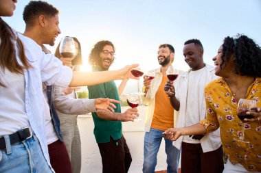 Bir grup çok ırklı mutlu arkadaş güneşli günün tadını çıkarıyorlar. Dans ediyorlar ve dışarıda kırmızı şarap içiyorlar. Genç milenyum insanları tatillerde teras partisini kutlarken eğleniyor.