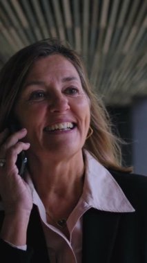 Dikey. Olgun Kafkasyalı resmi iş kadını dışarıda neşeli bir ifadeyle rahatça cep telefonuyla konuşuyor. Ofis işi molasında telefonuna cevap veren profesyonel sarışın kadın.